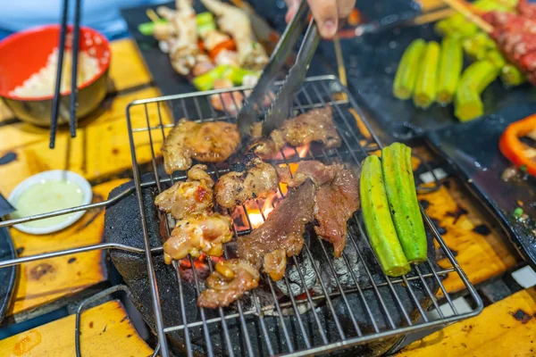 Mano umana con pinze e carne alla griglia sulla stufa a carbone — Foto Stock