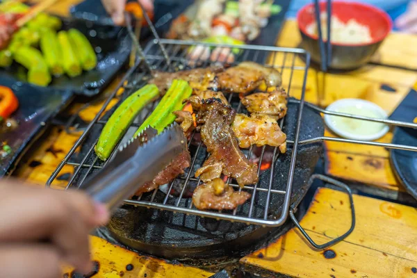 Man grilling okra vegetable and meat slices on charcoal stove — Stok fotoğraf