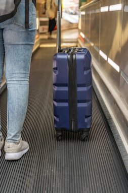 Havaalanı yürüyen merdiveninde valiz taşıyan bir kadının yakın plan fotoğrafı.