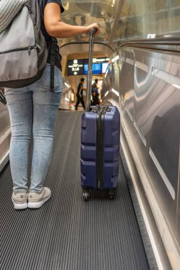 Havaalanındaki yürüyen merdivende kadın sırt çantalı birinin dikey fotoğrafı.