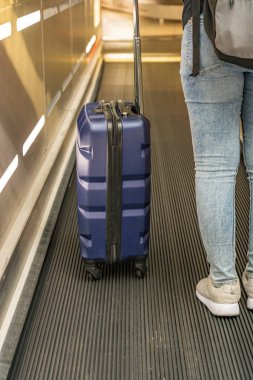 Havaalanındaki yürüyen merdivende el çantası taşıyan genç bir yolcu.