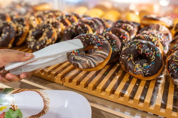 Hand plukken chocolade donut door klem bij bakkerij — Stockfoto