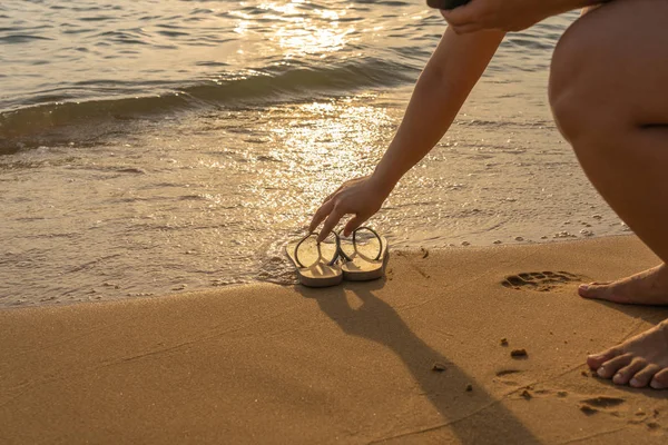 Frau nimmt Pantoffel am friedlichen Strand im Sonnenuntergang — Stockfoto