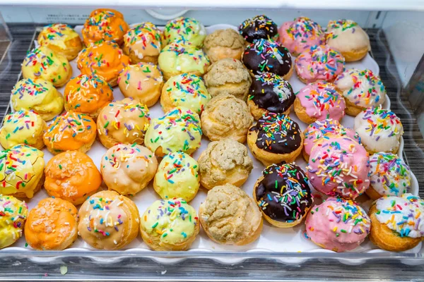 Puffy choux pastry with multicolored sugar icing topping on tray — Stock Photo, Image