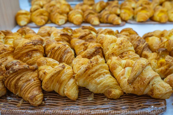 Pilha de croissants de queijo inchado na bandeja de vime na padaria — Fotografia de Stock