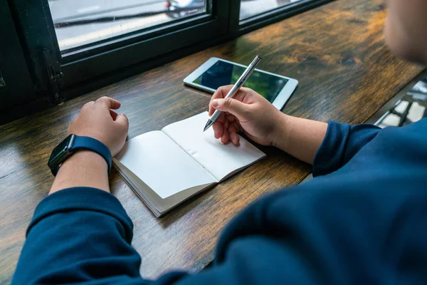 Kvinna hålla penna och skriva på anteckningsbok bredvid tablett — Stockfoto