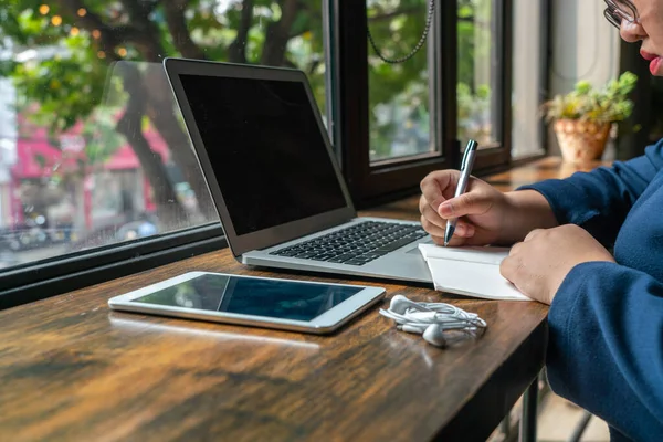 Mujer asiática escribiendo cuaderno junto a la computadora portátil y tableta — Foto de Stock