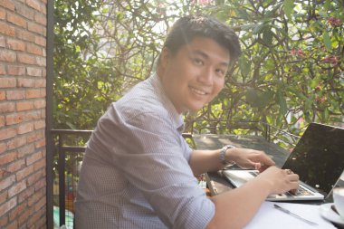 Genç Asyalı serbest çalışan adam dizüstü bilgisayarla çalışıyor.