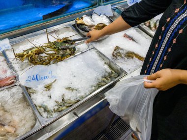 Kadın süpermarketteki deniz ürünleri standından donmuş kerevit alıyor.