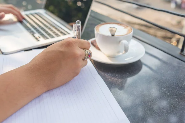 Empresario escribiendo portátil a mano izquierda, escribiendo nota a mano derecha — Foto de Stock