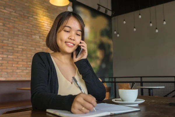 Asian lady write notes, answer phone call in the coffee shop