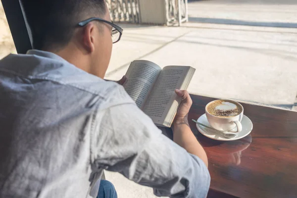 A fiatalember olvasókönyv és iszik kávé — Stock Fotó