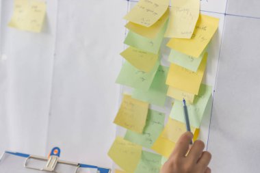 İnsan eli kalem tutarak yapışkan nota işaret ediyor.