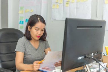 İş yerindeki Asyalı ofis çalışanı, günlük kıyafet giyip mali belgeler okuyor.