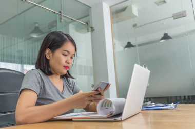 Akıllı telefon kullanan ve şirket ofisinde çalışan bir iş kadını.