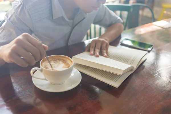 Ludzka dłoń trzyma otwartą książkę i miesza kawę — Zdjęcie stockowe