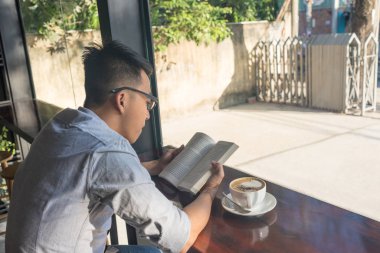 Genç öğrenci kitap okuyor ve kahve içiyor.