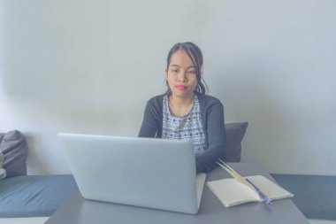 Asyalı kadın kanepede oturuyor ve dizüstü bilgisayarla çalışıyor.