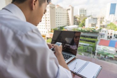 Genç Asyalı işadamı balkonda akıllı telefon kullanıyor.