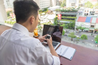 Genç adam dizüstü bilgisayar ve akıllı telefon kullanıyor.