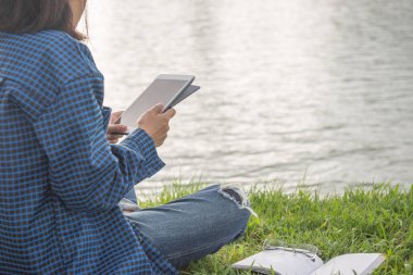 Tablet kullanan ve kitap okuyan genç bir kız.