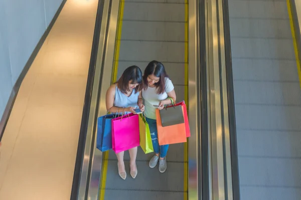 Young girls holding shopping paper bags with escalator background — 스톡 사진