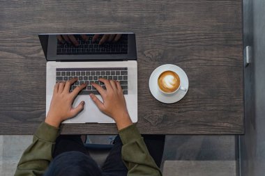 Kapüşonlu serbest çalışanın dizüstü bilgisayarla çalışmasını gösteren hava görüntüsü.