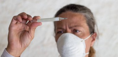 Grip virüsü ve koronavirüsü önlemek için termometresi ve çene bağı olan yetişkin bir kadın.