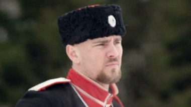 Kar kış manzara içinde bir kılıç sallanan kazak giysili genç bir adam.