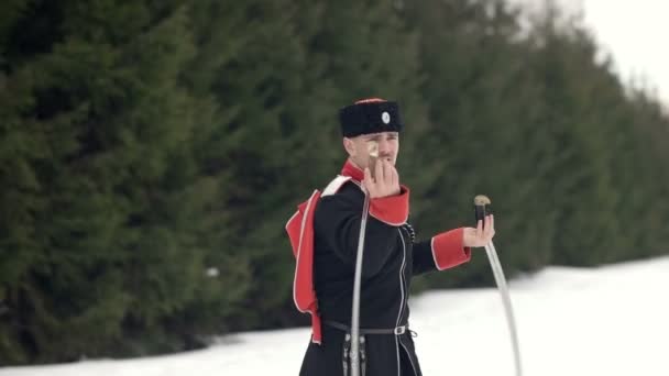 Un jeune homme en costume cosaque balançant une épée dans un paysage hivernal dans la neige . — Video