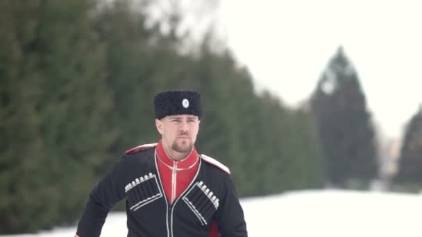 Un joven con ropa cosaca balanceando una espada en un paisaje invernal en la nieve . — Vídeos de Stock