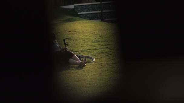 用手机在手躺在绿色的草坪在城市公园骑单车自行车女子 — 图库视频影像