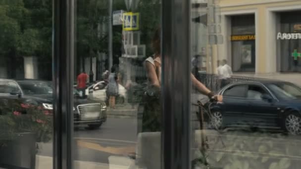 Αντανάκλαση στο παράθυρο γυναίκα ιππασία ποδήλατο στο δρόμο της πόλης σε φόντο κτίρια — Αρχείο Βίντεο