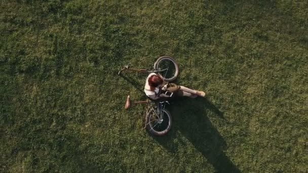 Drone vista ciclista mujer acostado en la hierba verde y el uso de teléfono móvil — Vídeo de stock