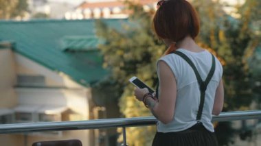 Genç kadın Kızıl saçlı holding ve cep telefonuyla arkadan görünüm