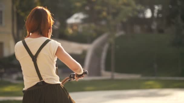 Röd haired kvinna cyklist cykla i city park tillbaka se — Stockvideo