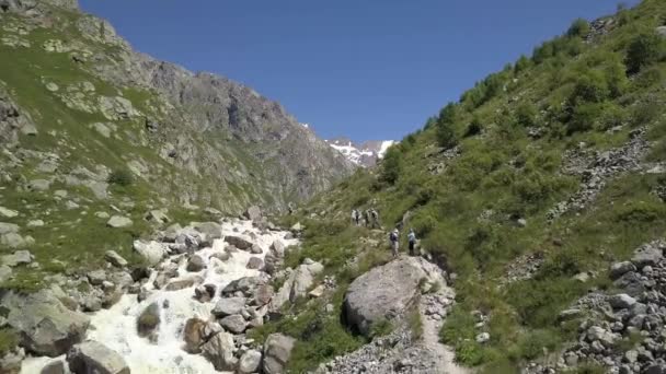 Туристична група, що йде по гірській стежці вздовж швидкої річки. сходження на гору — стокове відео