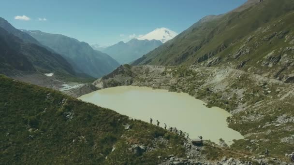 Туристическая группа, гуляющая по горам с видом на озеро и вершины. Горная природа — стоковое видео