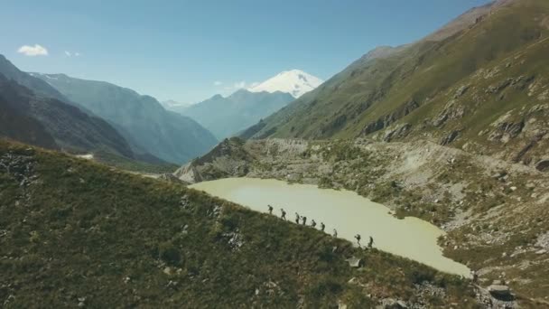 Mendaki orang berjalan di jalur pegunungan dengan pemandangan danau dan puncak salju — Stok Video