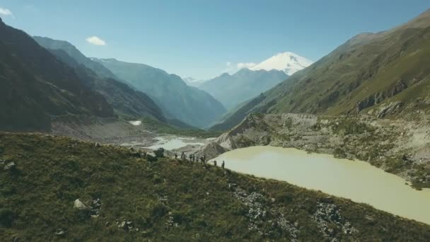 Туристическая группа стоит на краю горы на фоне горного озера — стоковое видео