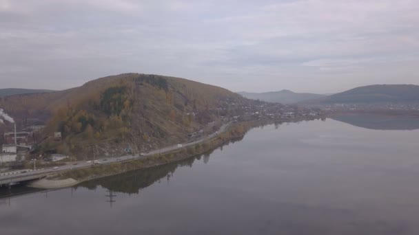 Voitures panoramiques et truques se déplaçant sur le pont fluvial par ville sur fond de montagne — Video