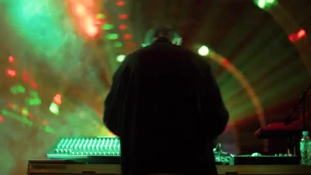 Чоловік діджей грає музику на тумбочці в нічному клубі на яскравому фоні освітлення — стокове відео