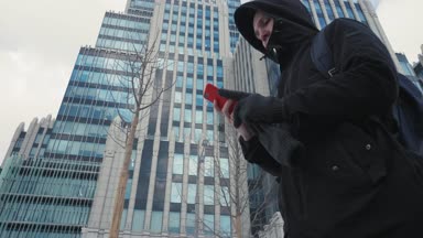 Adam siyah ceket ve cep telefonuyla ve şehir sokak yürüyüş sırt çantası