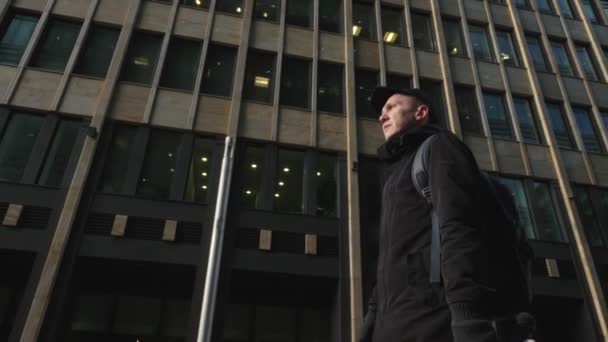 Man in zwarte pet en vest met rugzak lopen op stedelijke straat moderne stad — Stockvideo