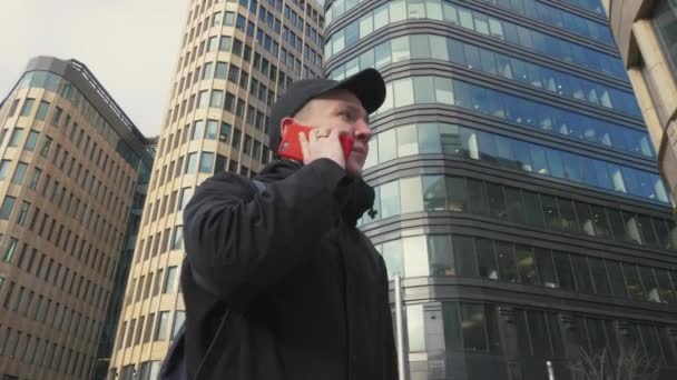 Mannen i svart keps prata via mobiltelefon under promenader på urban street — Stockvideo