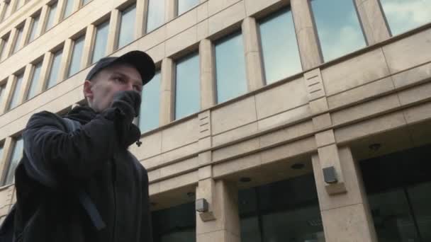 Человек в черной куртке дышит на руках в перчатках, чтобы согреться в холодный день — стоковое видео
