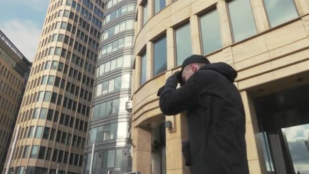 Человек в черной кепке идет по городской улице и машет рукой, чтобы поприветствовать — стоковое видео