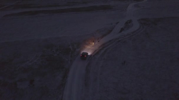 El hombre corriendo con el perro a lo largo de la carretera de invierno y el coche detrás de ellos por la noche — Vídeos de Stock