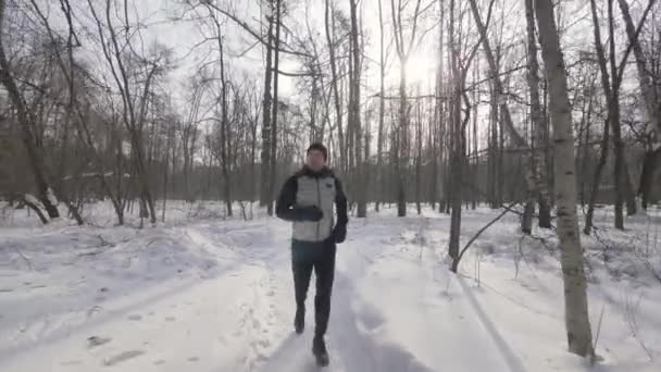 Портрет спортсмена біжить в зимовому лісі крупним планом. Зимові пробіжки в міському парку — стокове відео
