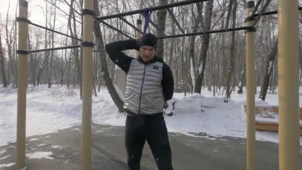 Hombre atleta haciendo ejercicio en cuclillas con expansor deportivo en campo de deportes de invierno — Vídeo de stock